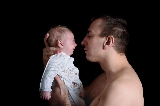 Père tenant son nouveau-né. Amour et tendresse des pères. Fond noir.