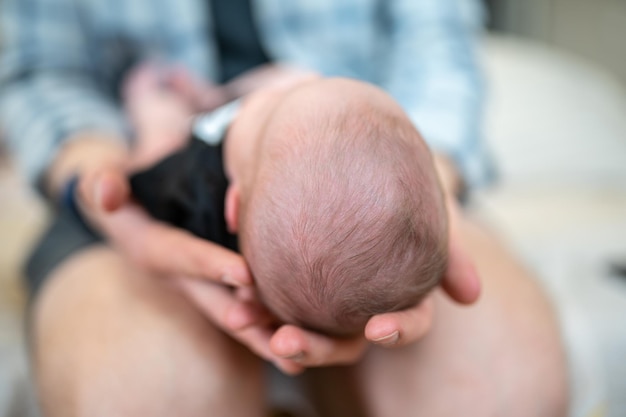 Le père tient le nouveau-né sur ses genoux, la tête tournée vers la caméra Se concentrer sur la tête de l'enfant