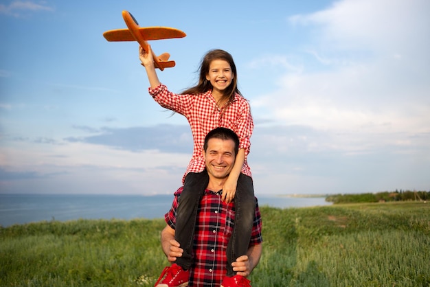 Le père tient sur ses épaules une petite fille sa fille marche dans le champ sur le fond du ciel jouant avec un modèle réduit d'avion