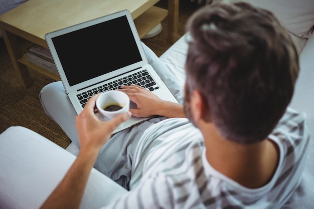 Père utilisant un ordinateur portable tout en buvant un café dans le salon