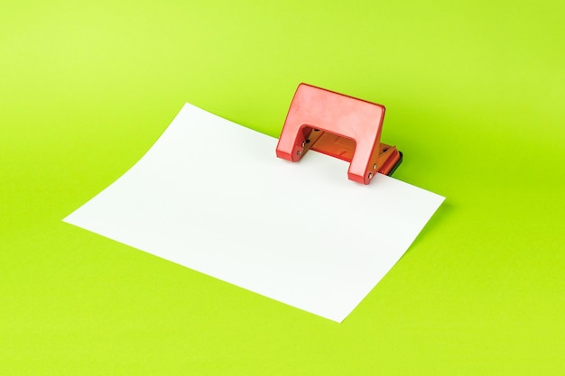 Une perforatrice rouge avec une feuille de papier blanche sur fond vert