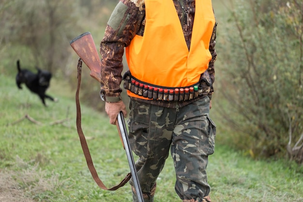 Période de chasse, saison d'automne ouverte. Un chasseur avec un fusil à la main en vêtements de chasse dans la forêt d'automne à la recherche d'un trophée. Un homme se tient debout avec des armes et des chiens de chasse traquant le gibier.