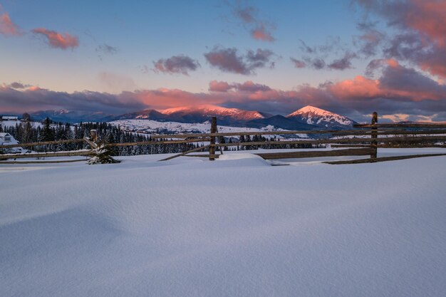 Périphérie du village alpin dans la lumière du soleil du coucher du soleil d'hiver collines enneigées et sapins