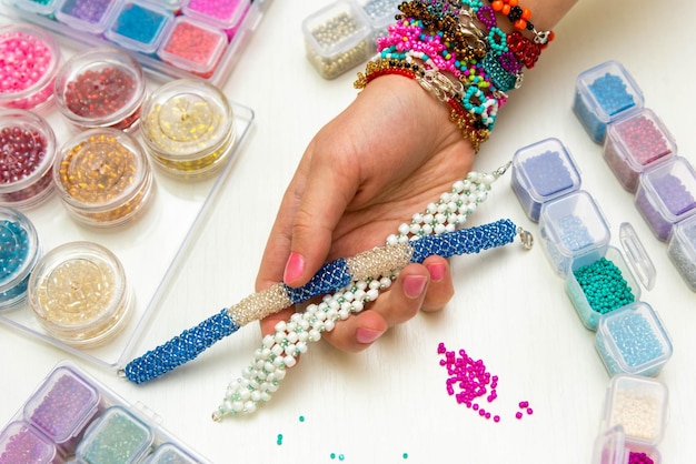 Photo perles pour enfants une main décorée d'un grand nombre de bracelets colorés tient un produit tissé en petites perles