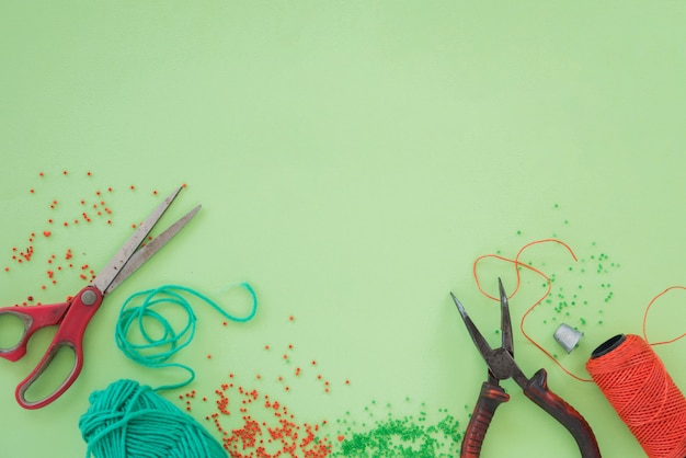 Perles Rouges Et Vertes; Ciseaux; Pince Et Bobine Sur Fond Vert