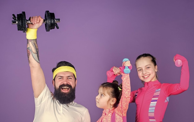 Permet de pratiquer Entraîneur sportif et petites filles renforçant leur force avec des haltères Père et filles faisant de l'exercice en cours de gym Entraînement familial heureux en cours de gym