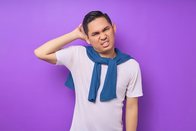 Perplexe, pensif, triste, jeune homme asiatique portant un t-shirt blanc se grattant la tête isolée sur fond violet concept de mode de vie des gens