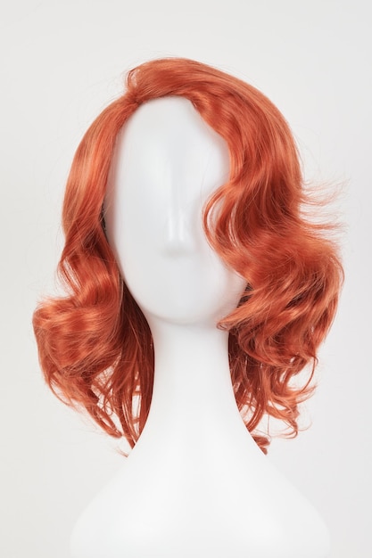 Perruque au gingembre d'aspect naturel sur la tête de mannequin blanc Cheveux de longueur moyenne avec des boucles ondulées sur le support de perruque en plastique isolé sur fond blanc vue de face