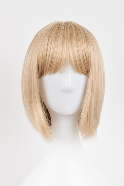 Perruque blonde d'apparence naturelle sur tête de mannequin blanc Coupe de cheveux courte sur le support de perruque en plastique isolé sur fond blanc vue avant