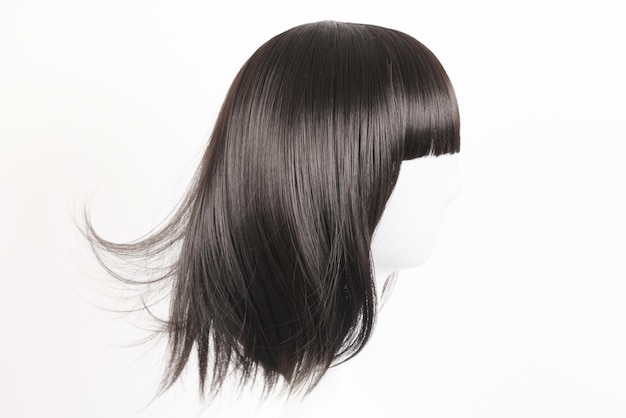 Perruque noire d'aspect naturel sur tête de mannequin blanc Cheveux raides de longueur moyenne avec une frange sur le porte-perruque en métal isolé sur fond blanc vue latérale