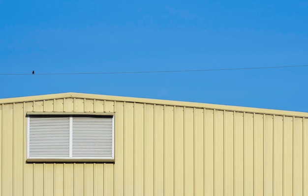 Persienne en aluminium sur mur d'entrepôt en acier ondulé jaune sur fond de ciel bleu