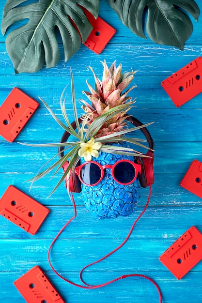 Personnage d'ananas hipster en lunettes de soleil rouges et écouteurs écoute de la musique