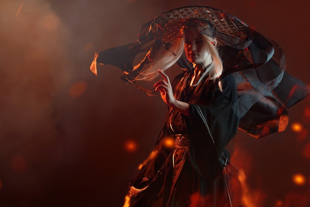 Photo un personnage de style asiatique dans un kimono et un chapeau de paille avec des rubans au milieu du feu