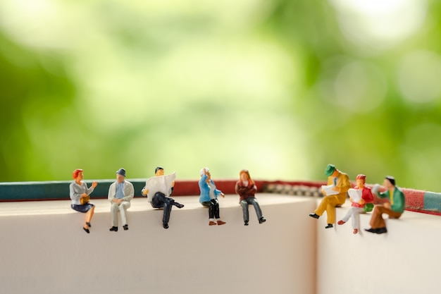 Personnages miniatures: groupe d'hommes d'affaires assis sur un livre.