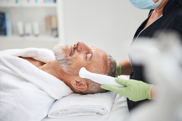 Personne âgée allongée sur une table de spa tout en ayant une procédure de photorajeunissement de la peau dans un salon