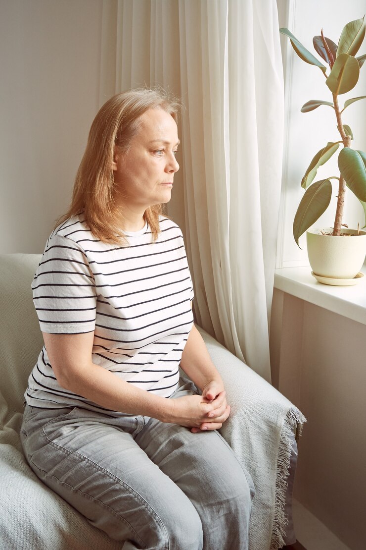 Une personne âgée triste est assise à la maison près de la fenêtre