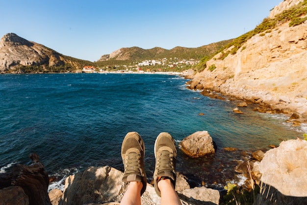 Une personne assise sur une falaise Pieds selfie de voyageur. Selfie de jambes en baskets vertes. Rochers et mer en arrière-plan Heure d'été en Crimée