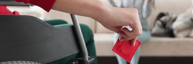 Une personne assise en fauteuil roulant tient un préservatif rouge dans sa main devant une femme assise