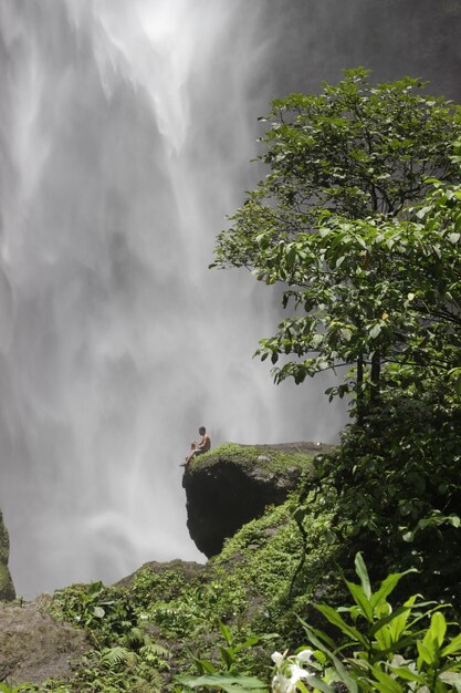 Photo personne assise sur un rocher près d'une cascade