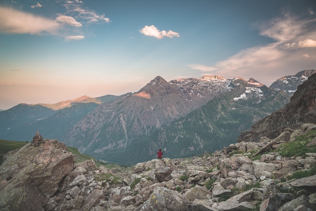 Une personne assise sur un terrain rocheux et regardant le lever du soleil dans les Alpes