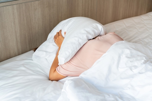 Personne au lit à l'aide d'un oreiller pour se couvrir la tête pour se cacher de la lumière du soleil