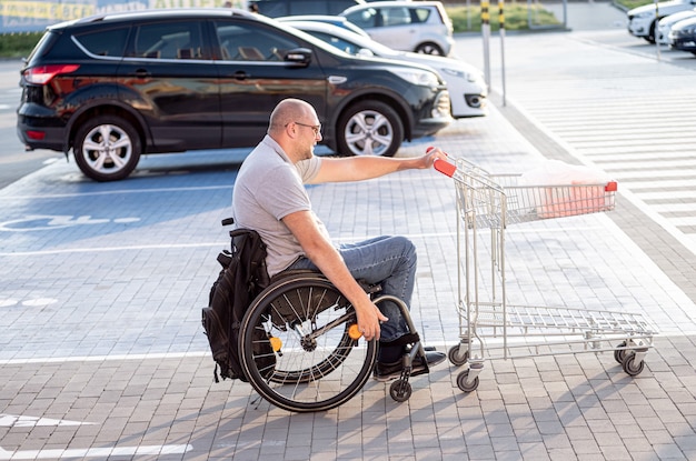 Personne ayant un handicap physique poussant le chariot devant lui au parking d'un supermarché