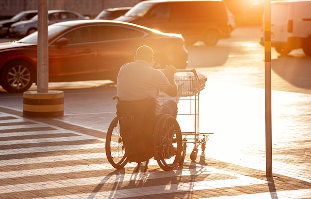 Personne ayant un handicap physique poussant le chariot devant lui au parking d'un supermarché