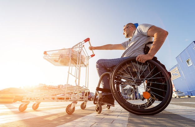 Personne ayant un handicap physique poussant le chariot devant lui au parking d'un supermarché