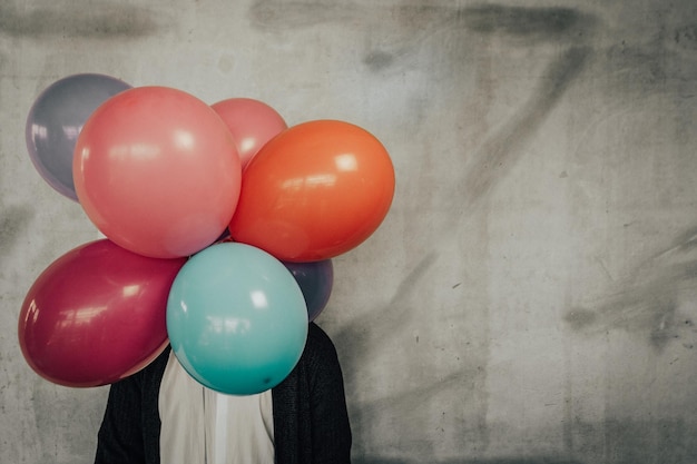 Personne avec des ballons colorés alors qu'elle se tient contre le mur