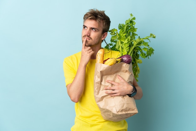 Personne blonde prenant un sac de plats à emporter isolé sur fond bleu ayant des doutes tout en regardant