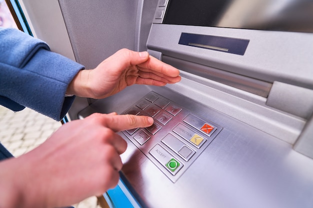 La personne compose et cache avec l'autre main pour des raisons de sécurité un code PIN sur le clavier de la banque ATM pour retirer de l'argent