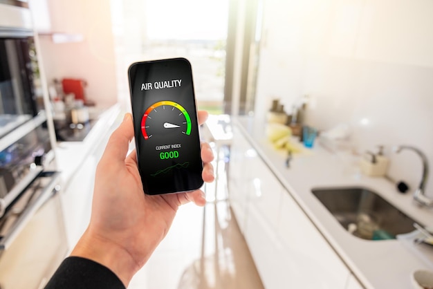 Personne dans la cuisine à la maison regardant l'indice de qualité de l'air sur son téléphone portable