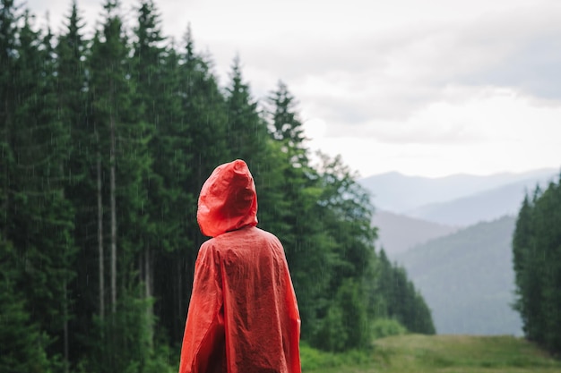 Une personne dans un imperméable rouge se tient sur la pluie dans les montagnes sur fond de paysage