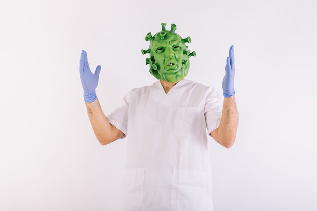 Personne déguisée en coronavirus avec masque en latex virus Covid19, portant un costume de médecin, ouvrant les bras, sur fond blanc
