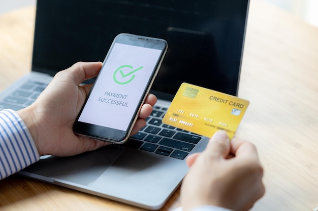 Une personne détient une carte de crédit pour payer en ligne Les paiements par carte de crédit peuvent être utilisés à la fois sur des ordinateurs portables et sur des téléphones portables Concept de paiement de biens et de services par carte de crédit