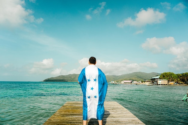 Une personne avec un drapeau du Honduras devant une mer et une île