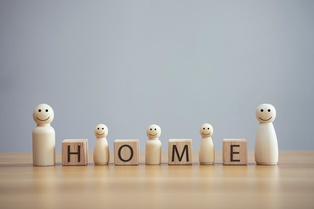 Une personne de famille en bois heureuse modèle un smiley avec un mot maison sur fond de table en cube de bois