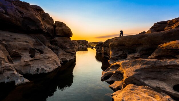 Personne sur des formations rocheuses par la mer contre le ciel au coucher du soleil