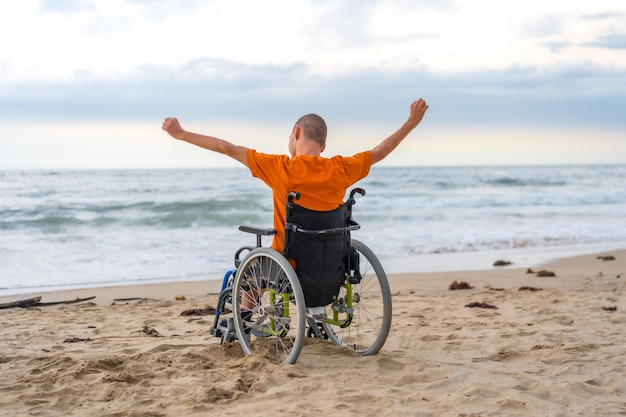 Une personne handicapée sur le dos dans un fauteuil roulant sur la plage avec les bras ouverts appréciant la liberté