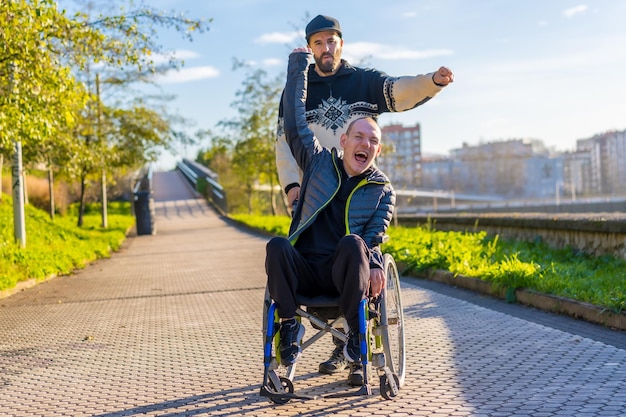 Personne handicapée en fauteuil roulant avec un ami fou de joie souriant profitant des bras levés vistoria profitant de la vie