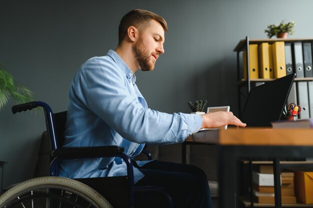 La personne handicapée en fauteuil roulant travaille au bureau à l'ordinateur Il est souriant et passionné par le flux de travail