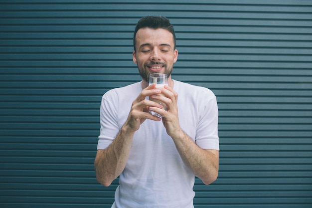 Une personne heureuse est debout et tient un verre de lait Il garde les yeux fermés et profite du moment. Isolé sur rayé