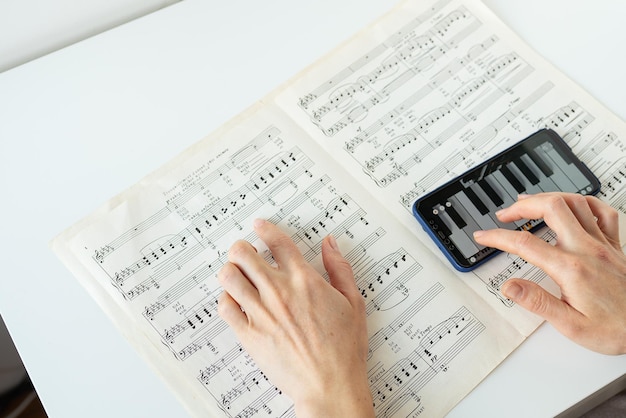 Photo une personne jouant une application de piano numérique sur un smartphone tout en lisant des partitions les mains sont visibles