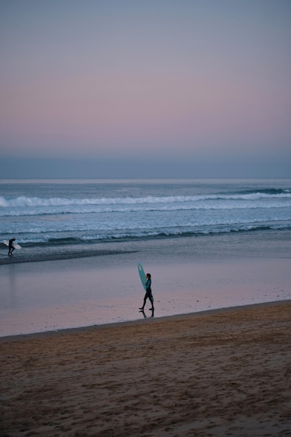 Une personne marchant sur une plage avec une planche de surf à la main.