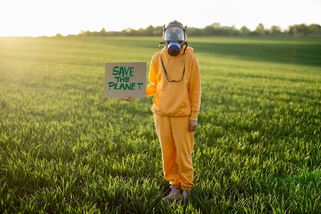 Une personne en masque à gaz tient un carton avec un appel pour sauver la planète