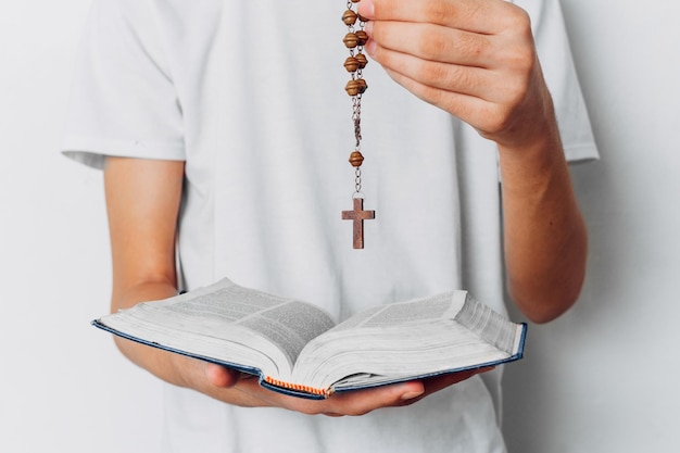 Personne méconnaissable tenant un chapelet et une bible catholique, concept de religion.