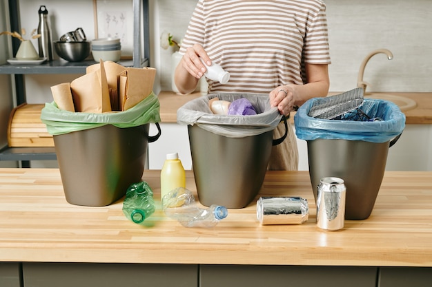 Une personne mettant une petite bouteille de yaourt en plastique dans une poubelle de cuisine