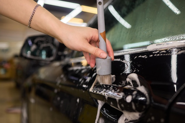 Une personne nettoie le pare-brise d'une voiture avec une brosse et de l'eau