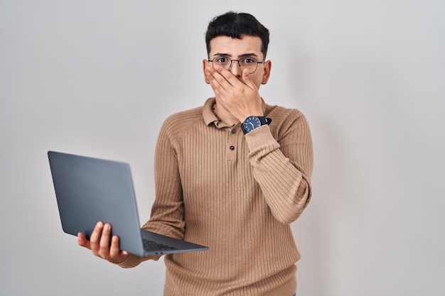 Personne non binaire utilisant un ordinateur portable choqué couvrant la bouche avec les mains pour un concept secret d'erreur