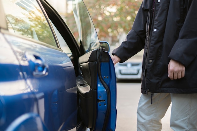 La personne ouvre la porte de la voiture bleue et s'assoit à l'intérieur